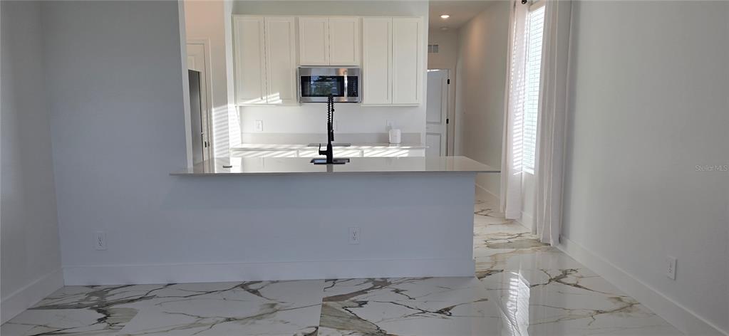 A kitchen features white cabinets, a stainless steel microwave, a breakfast bar, and marble-patterned flooring — 5560 MORANT BAY PATH, KISSIMMEE, FL