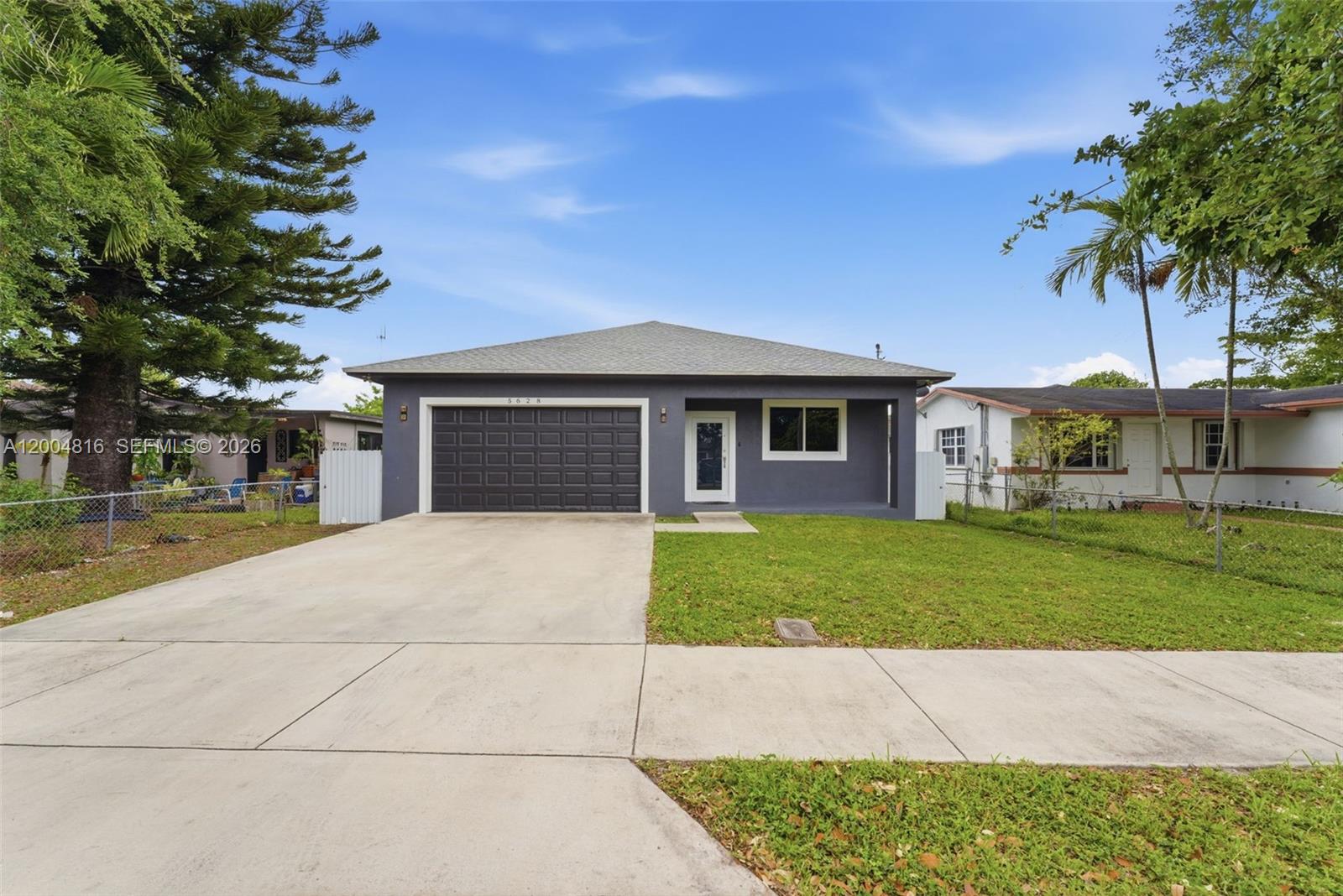 A gray single-story house features a dark garage door, a front door, and a concrete driveway — 5628 Flagler St, Hollywood FL 33023, HOLLYWOOD, FL