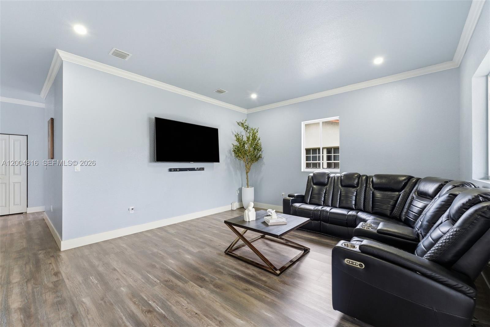 A living room features light blue walls, wood-look flooring, a wall-mounted television, and black leather seating — 5628 Flagler St, Hollywood FL 33023, HOLLYWOOD, FL
