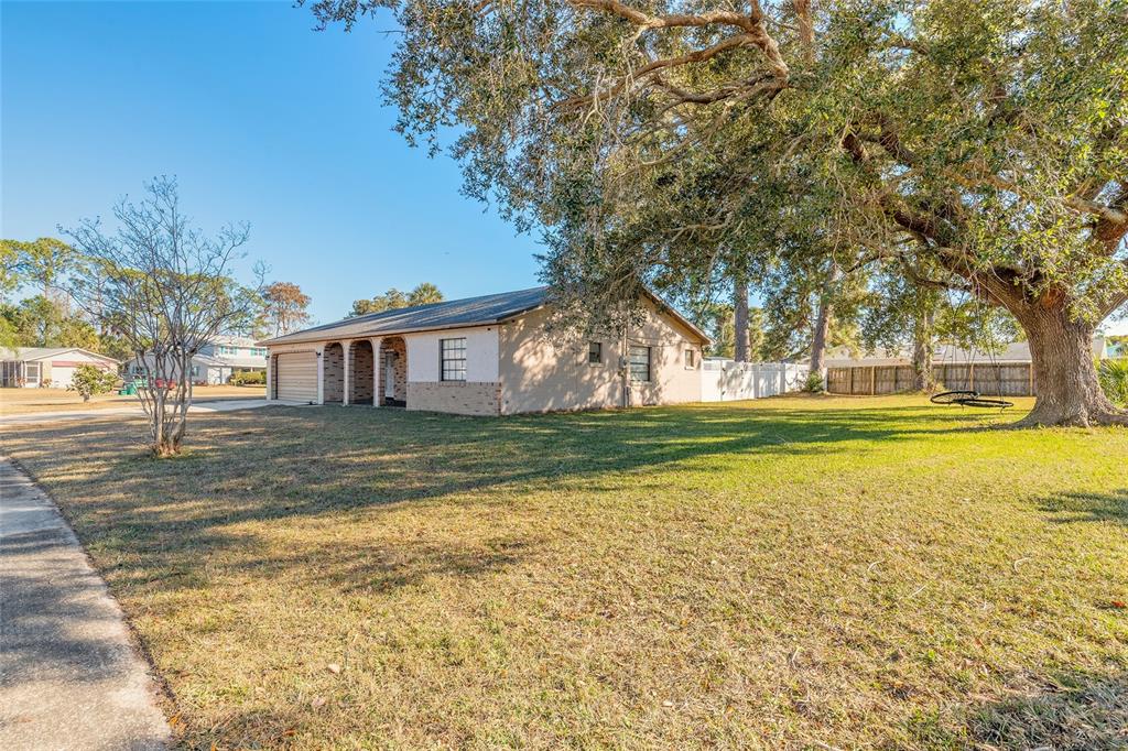 A single-story house with a tan exterior, attached garage, and large oak tree in front — 1210 MELLISA DRIVE, PORT ORANGE, FL