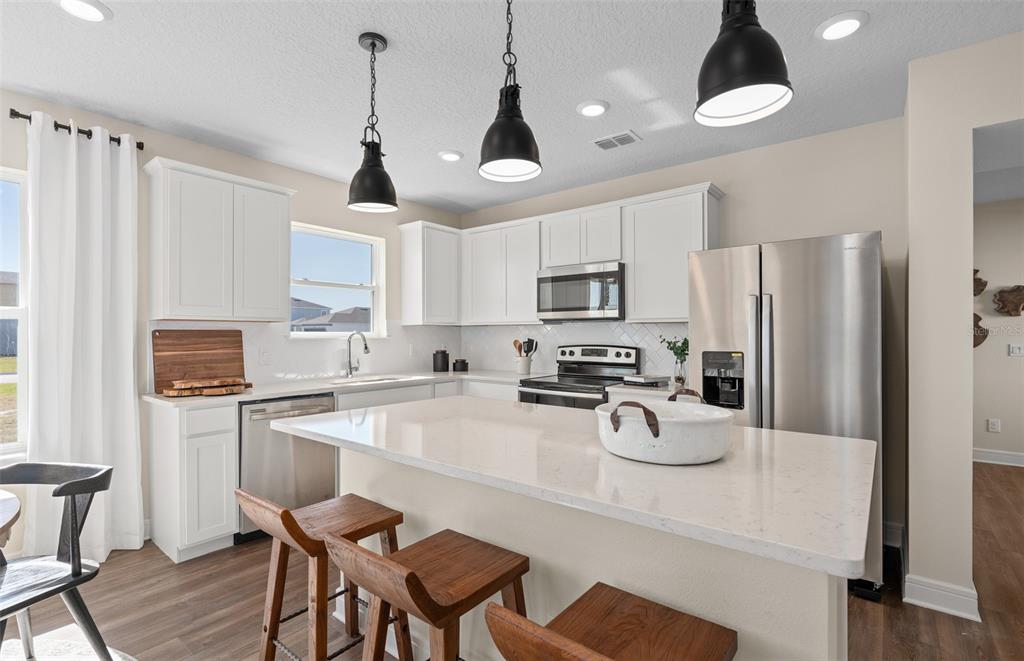 A modern kitchen features white cabinets, stainless steel appliances, a quartz island, and wooden stools — 2644 CLEAR NIGHT AVENUE DRIVE, KISSIMMEE, FL