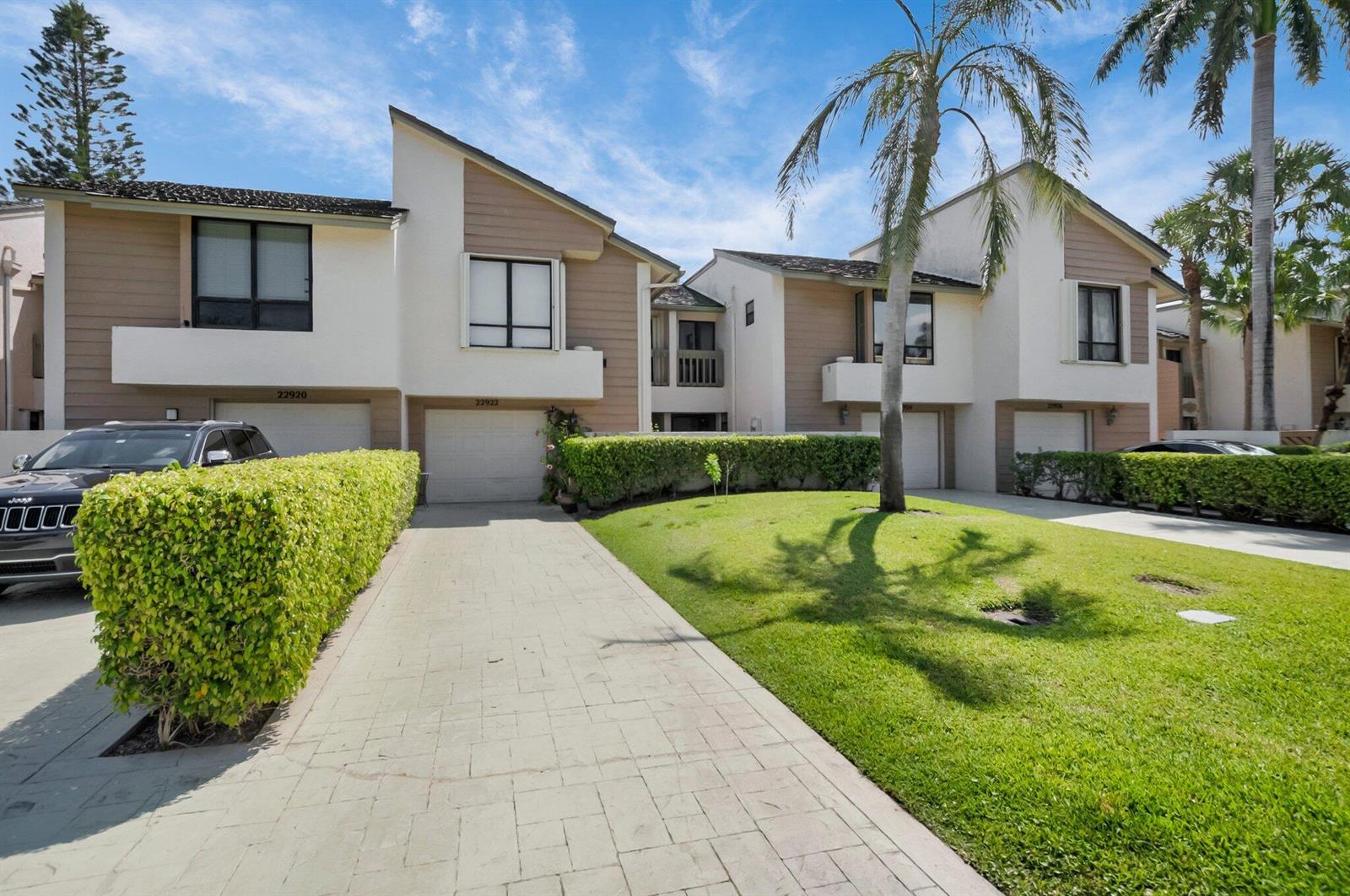 A two-story townhouse exterior with a paved driveway, green hedges, and a palm tree — 22922 Ironwedge Drive, Boca Raton FL 33433, BOCA RATON, FL