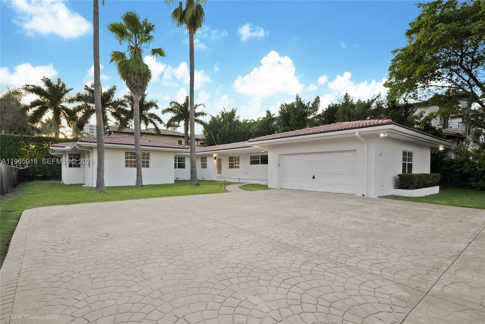 A single-story house with a paved driveway, garage, and landscaped flower beds at dusk — 52 Camden Dr, Bal Harbour FL 33154, BAL HARBOUR, FL