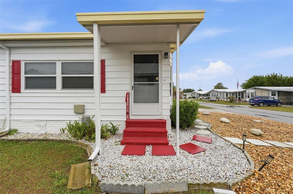 A white mobile home exterior features red steps, a covered entryway, and a gravel yard — 5027 FOREST CREST DRIVE, LAKELAND, FL