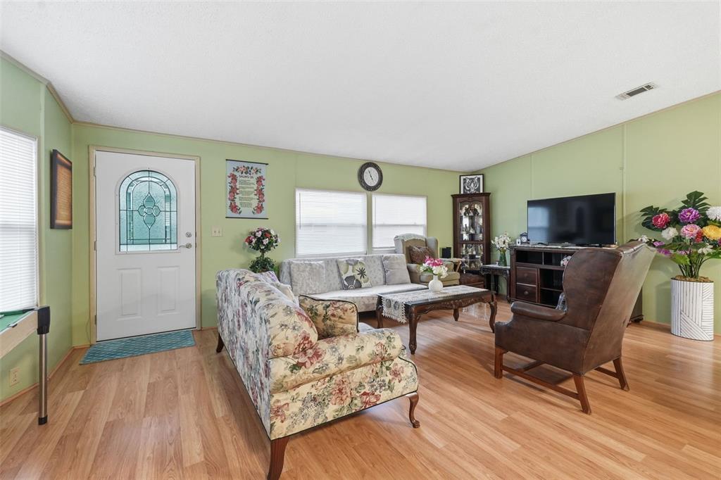 A living room features light green walls, wood-look flooring, a floral sofa, and a television — 5027 FOREST CREST DRIVE, LAKELAND, FL