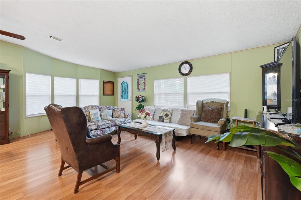 A living room with light green walls, wood-look flooring, and various pieces of furniture — 5027 FOREST CREST DRIVE, LAKELAND, FL