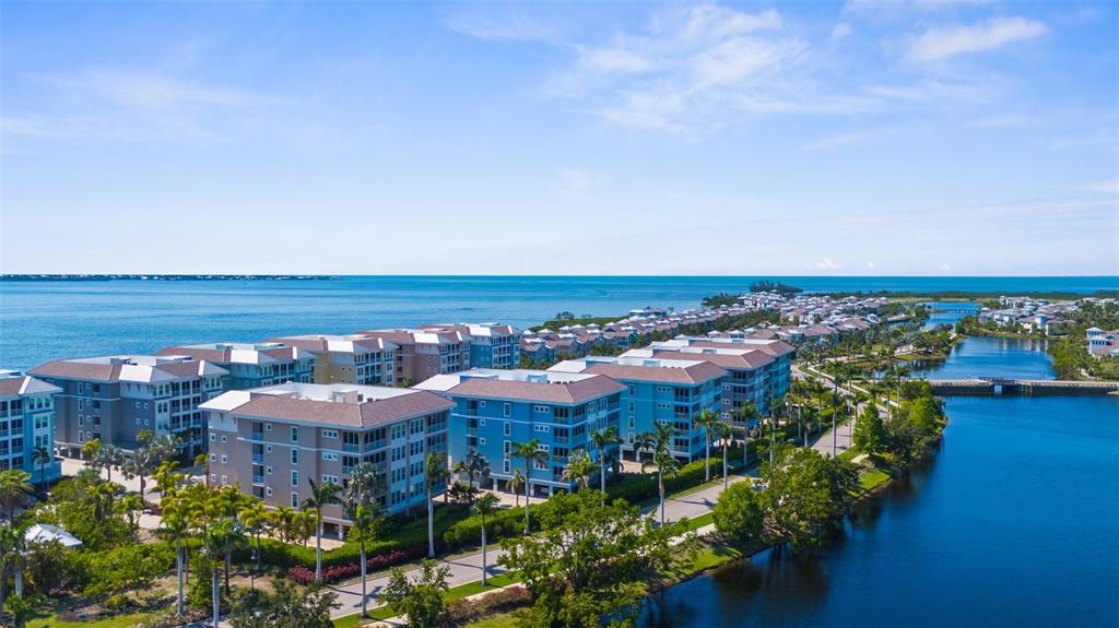 An aerial view shows multi-story apartment buildings situated between a blue bay and a canal — 395 ARUBA CIRCLE UNIT 401, BRADENTON, FL