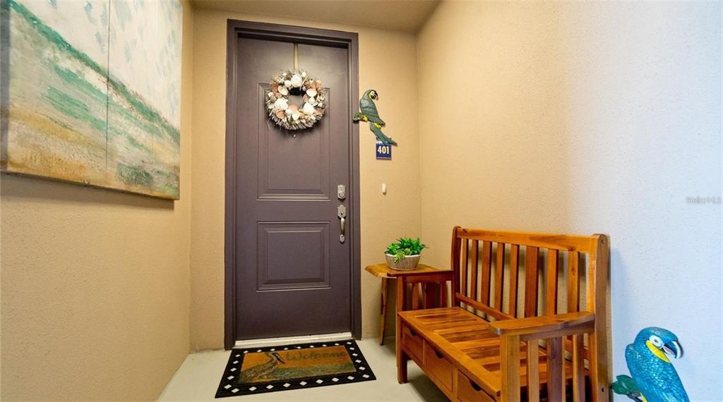 An entryway features a dark door with a wreath, a wooden bench, and parrot decor — 395 ARUBA CIRCLE UNIT 401, BRADENTON, FL