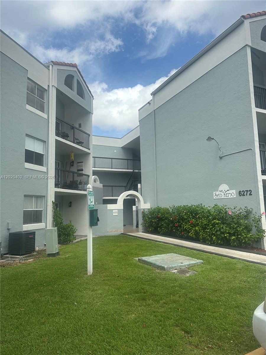 An exterior view of a multi-story apartment building with a grassy lawn and walkway — 6272 NW 186th St # 212, Hialeah FL 33015, HIALEAH, FL
