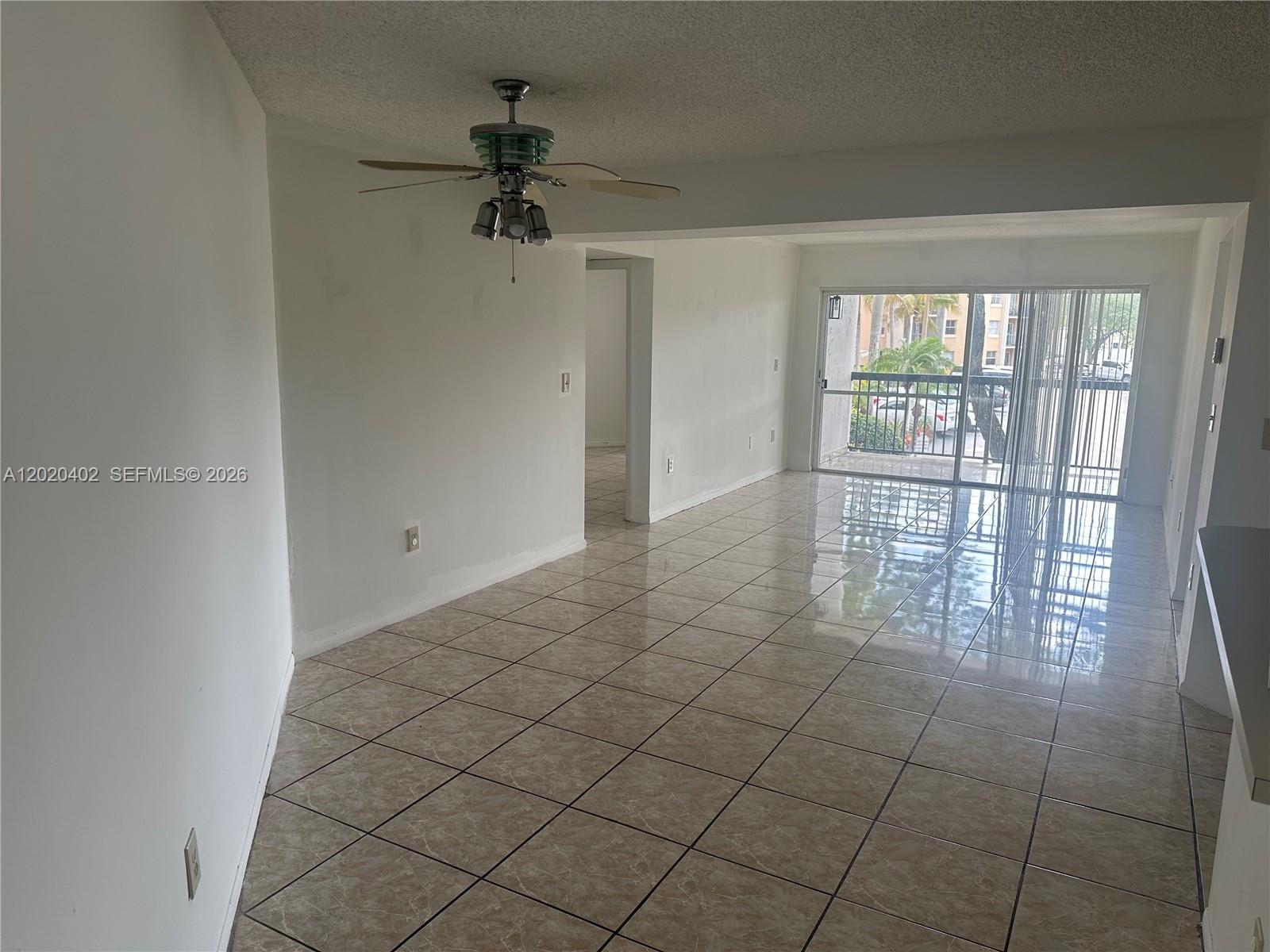 An empty room features beige tile flooring, a ceiling fan, and a sliding glass door — 6272 NW 186th St # 212, Hialeah FL 33015, HIALEAH, FL