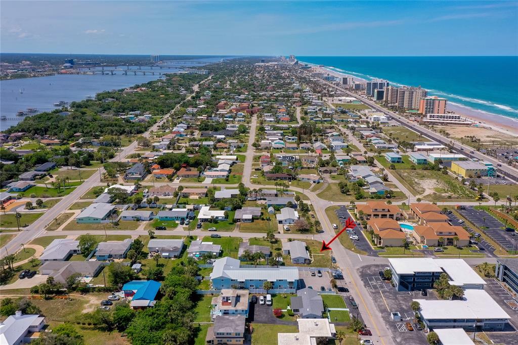 An aerial view shows a coastal neighborhood with houses, apartment buildings, and a nearby beach — 130 BOYNTON BOULEVARD, DAYTONA BEACH, FL