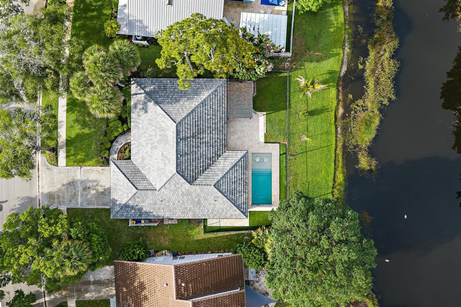 Aerial view of a house with a gray roof, swimming pool, and backyard facing a canal — 18169 Lake Bend Drive, Jupiter FL 33458, JUPITER, FL