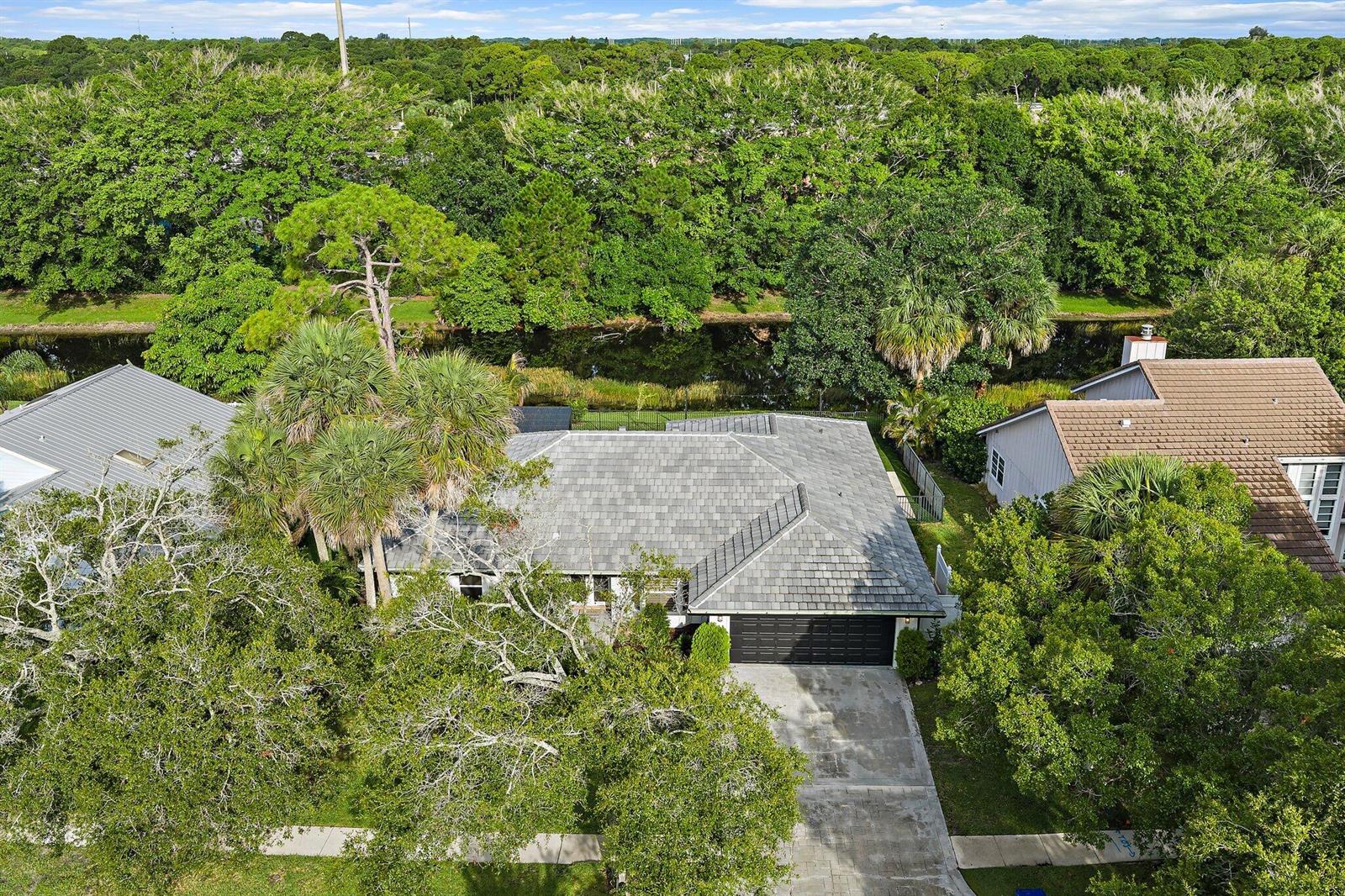 An aerial view shows a house with a gray roof, garage, and backyard canal — 18169 Lake Bend Drive, Jupiter FL 33458, JUPITER, FL