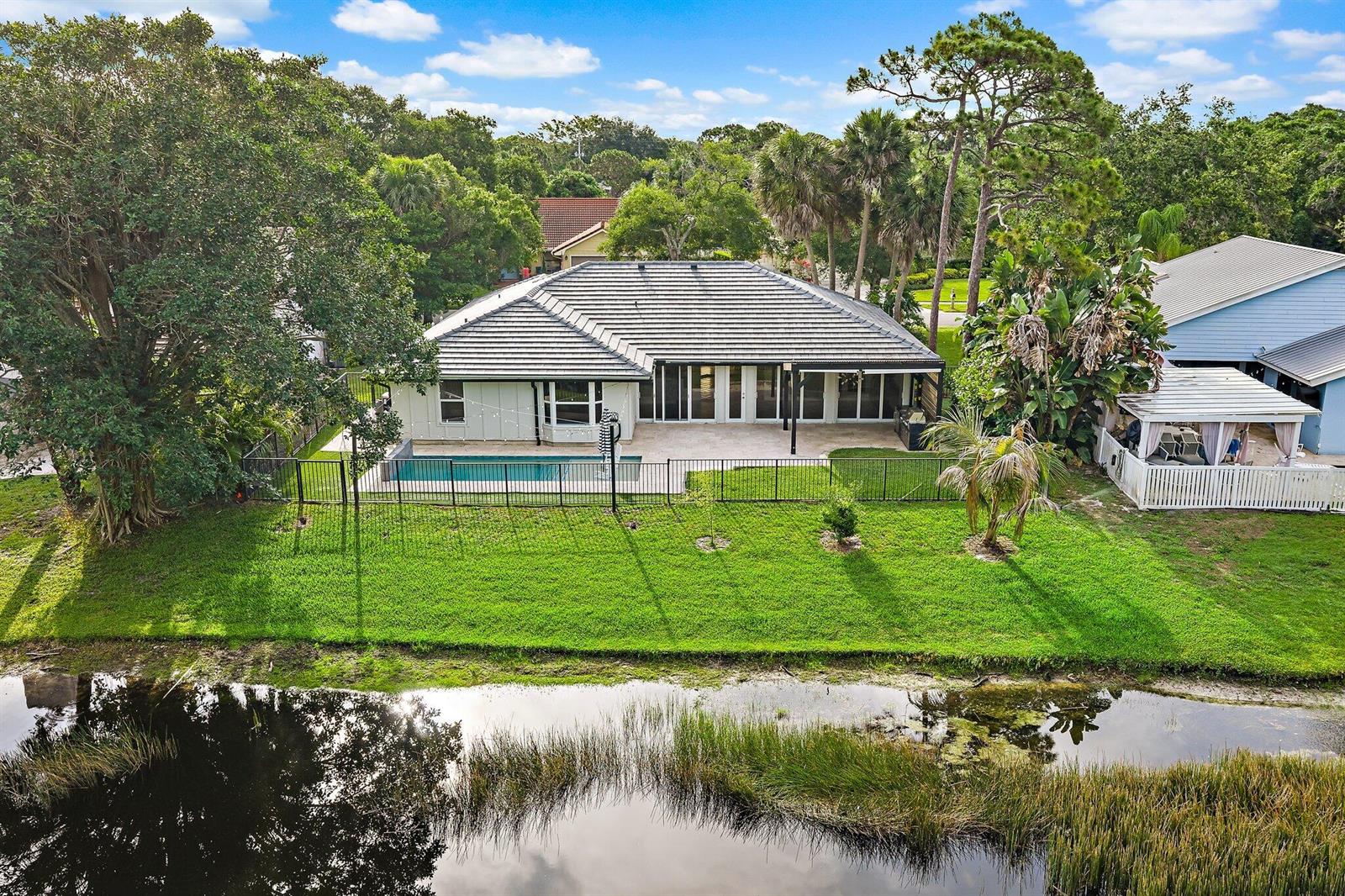 An aerial view of a house with a swimming pool, fenced yard, and canal — 18169 Lake Bend Drive, Jupiter FL 33458, JUPITER, FL