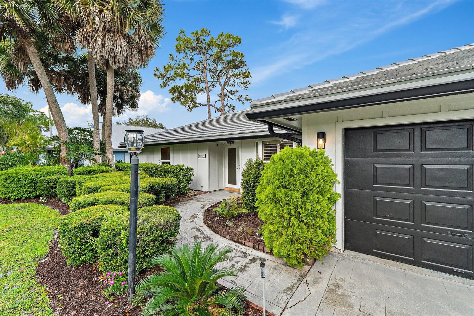 A paved walkway leads to the front entrance of a house with a dark garage — 18169 Lake Bend Drive, Jupiter FL 33458, JUPITER, FL