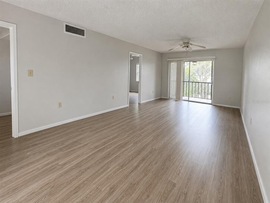 An empty living room features light wood-look flooring, a ceiling fan, and a sliding glass door — 112 CYPRESS COURT UNIT 112, OLDSMAR, FL