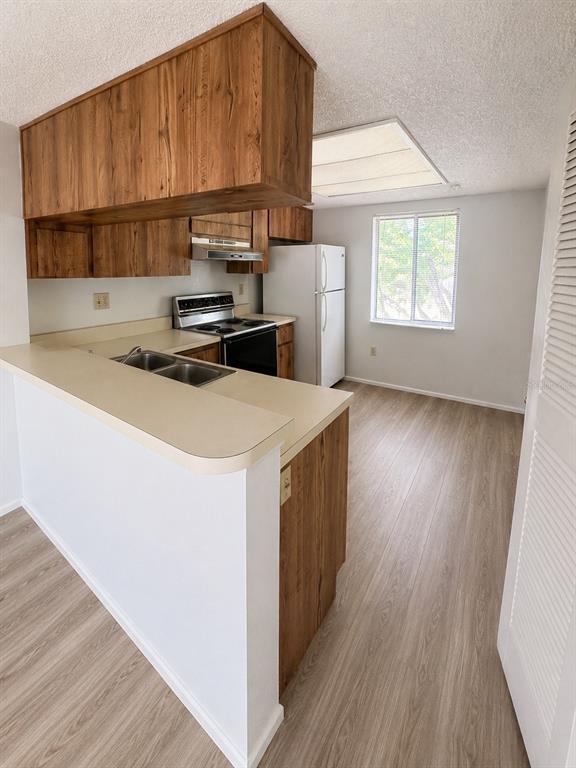 A kitchen features wood cabinets, a white refrigerator, a stove, and light-colored laminate flooring — 112 CYPRESS COURT UNIT 112, OLDSMAR, FL