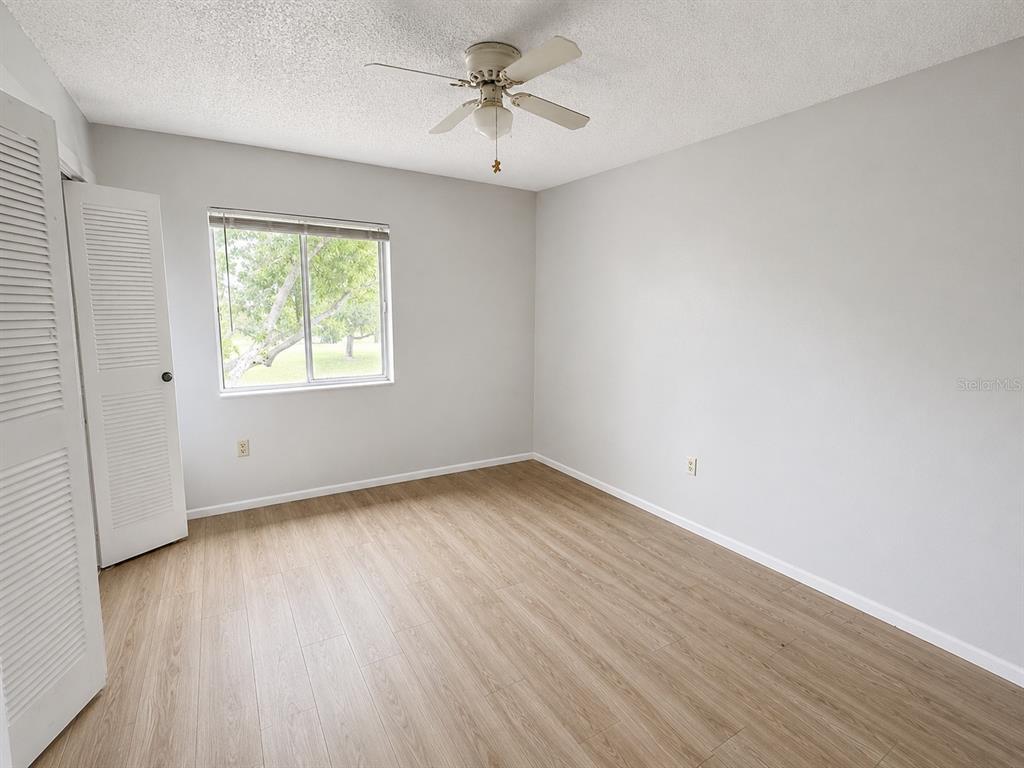 An empty bedroom features light gray walls, wood-look flooring, a ceiling fan, and louvered closet doors — 112 CYPRESS COURT UNIT 112, OLDSMAR, FL