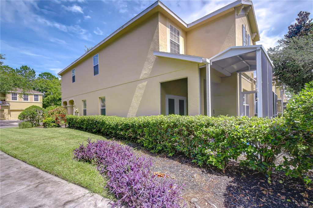 A two-story yellow house features a screened-in patio, a manicured hedge, and purple landscaping — 9328 STONE RIVER PLACE, RIVERVIEW, FL