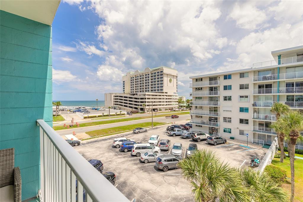 A balcony view overlooks a parking lot, nearby buildings, and the ocean in the distance — 2727 N ATLANTIC AVENUE UNIT 4190, DAYTONA BEACH, FL