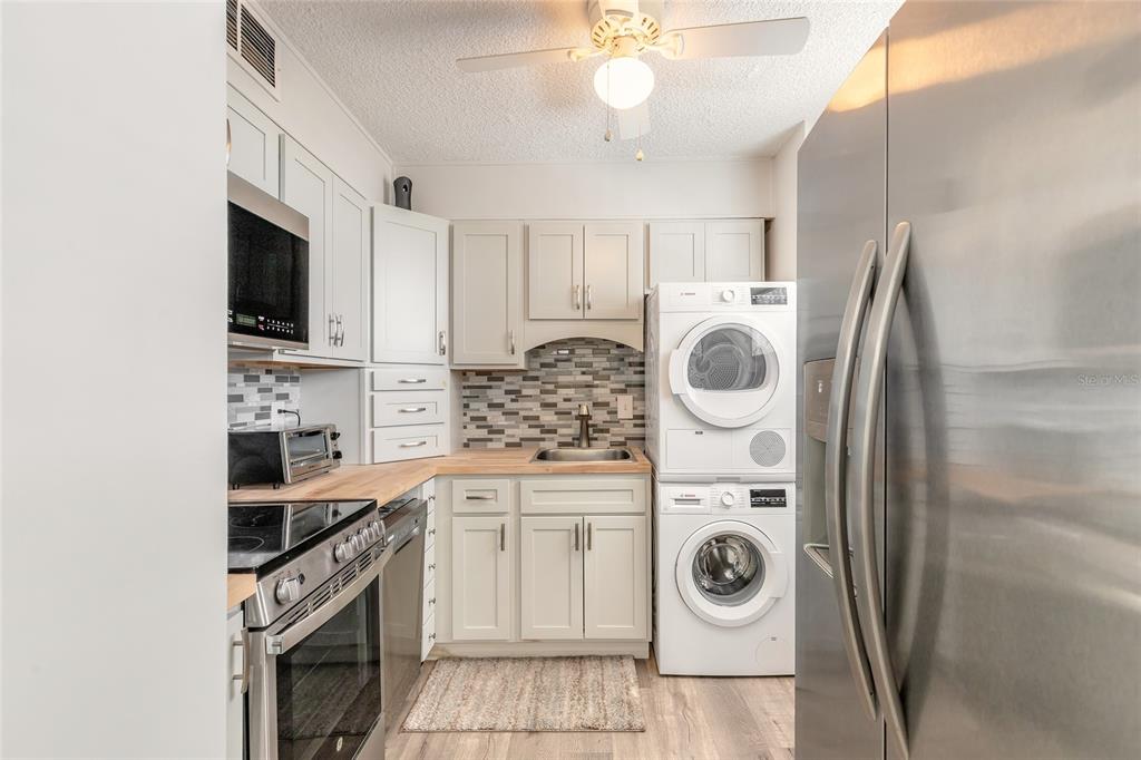 A kitchen features light-colored cabinetry, stainless steel appliances, a stacked washer-dryer, and wood countertops — 2727 N ATLANTIC AVENUE UNIT 4190, DAYTONA BEACH, FL