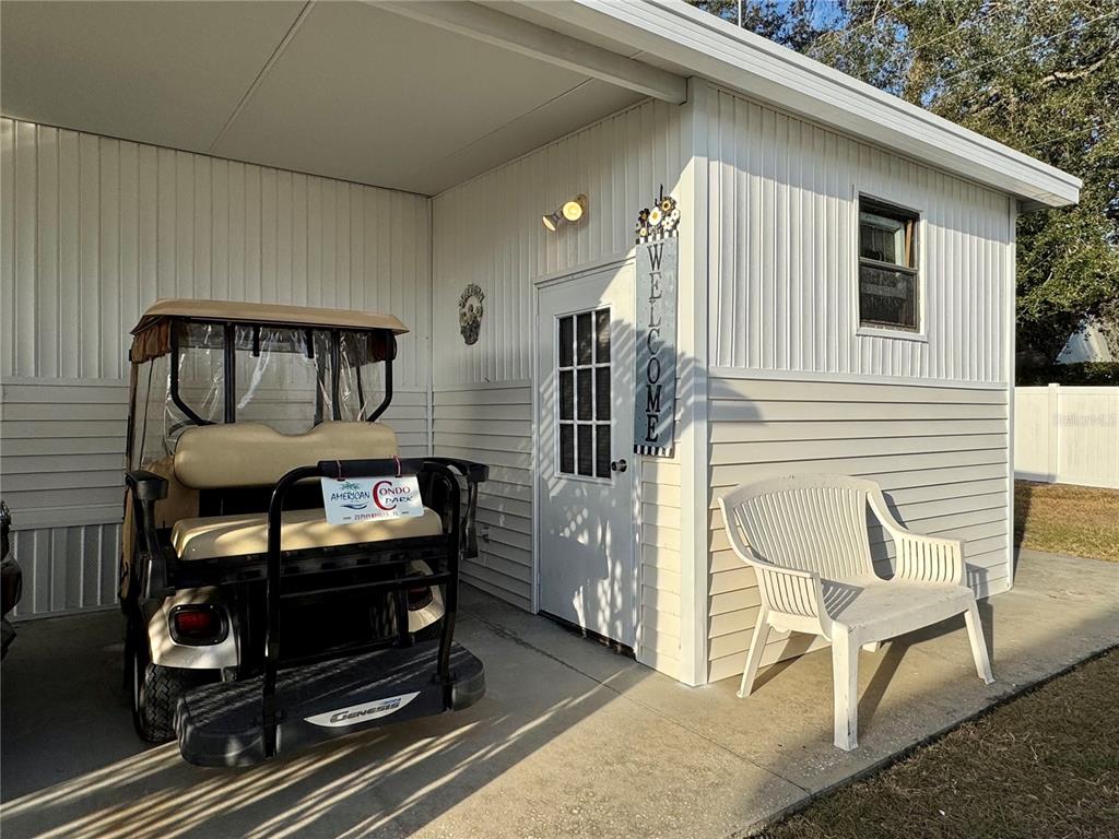 A golf cart is parked on a concrete patio next to a white house entrance — 4920 BRITNI WAY UNIT 074, ZEPHYRHILLS, FL