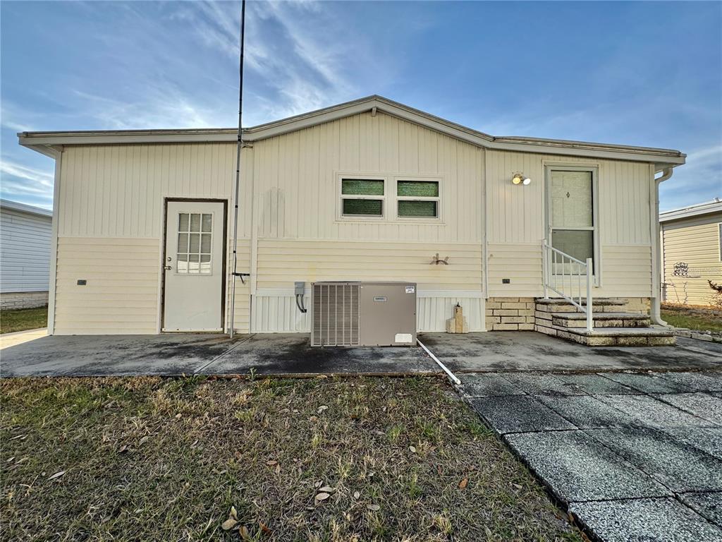 The exterior of a light-colored mobile home features a concrete patio and an HVAC unit — 4920 BRITNI WAY UNIT 074, ZEPHYRHILLS, FL