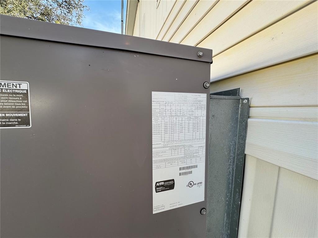 A close-up view of an outdoor HVAC unit's metal casing with a technical specification label — 4920 BRITNI WAY UNIT 074, ZEPHYRHILLS, FL