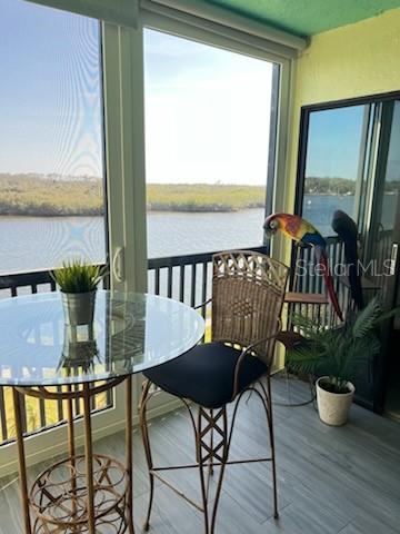 A sunroom features a glass-topped bistro table, a wicker chair, and a view of water — 8150 BRENT STREET UNIT 734, PORT RICHEY, FL