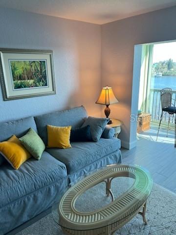 A living room features a gray sofa, a glass-topped coffee table, and a balcony overlooking water — 8150 BRENT STREET UNIT 734, PORT RICHEY, FL