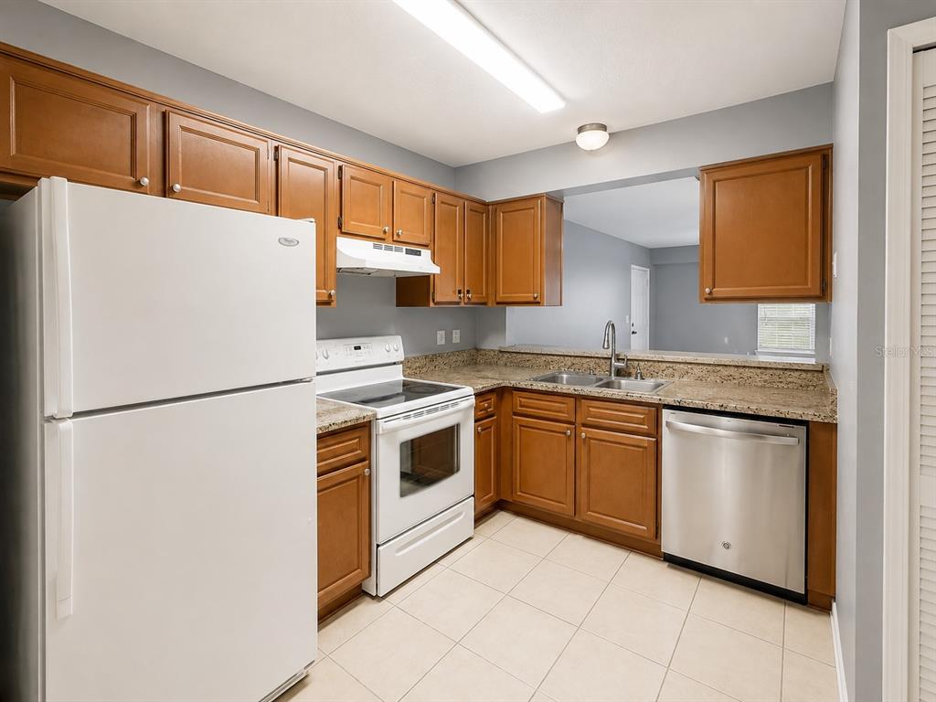 A kitchen features wood cabinets, granite countertops, a white refrigerator, and stainless steel appliances — 112 RESERVE CIRCLE UNIT 100, OVIEDO, FL