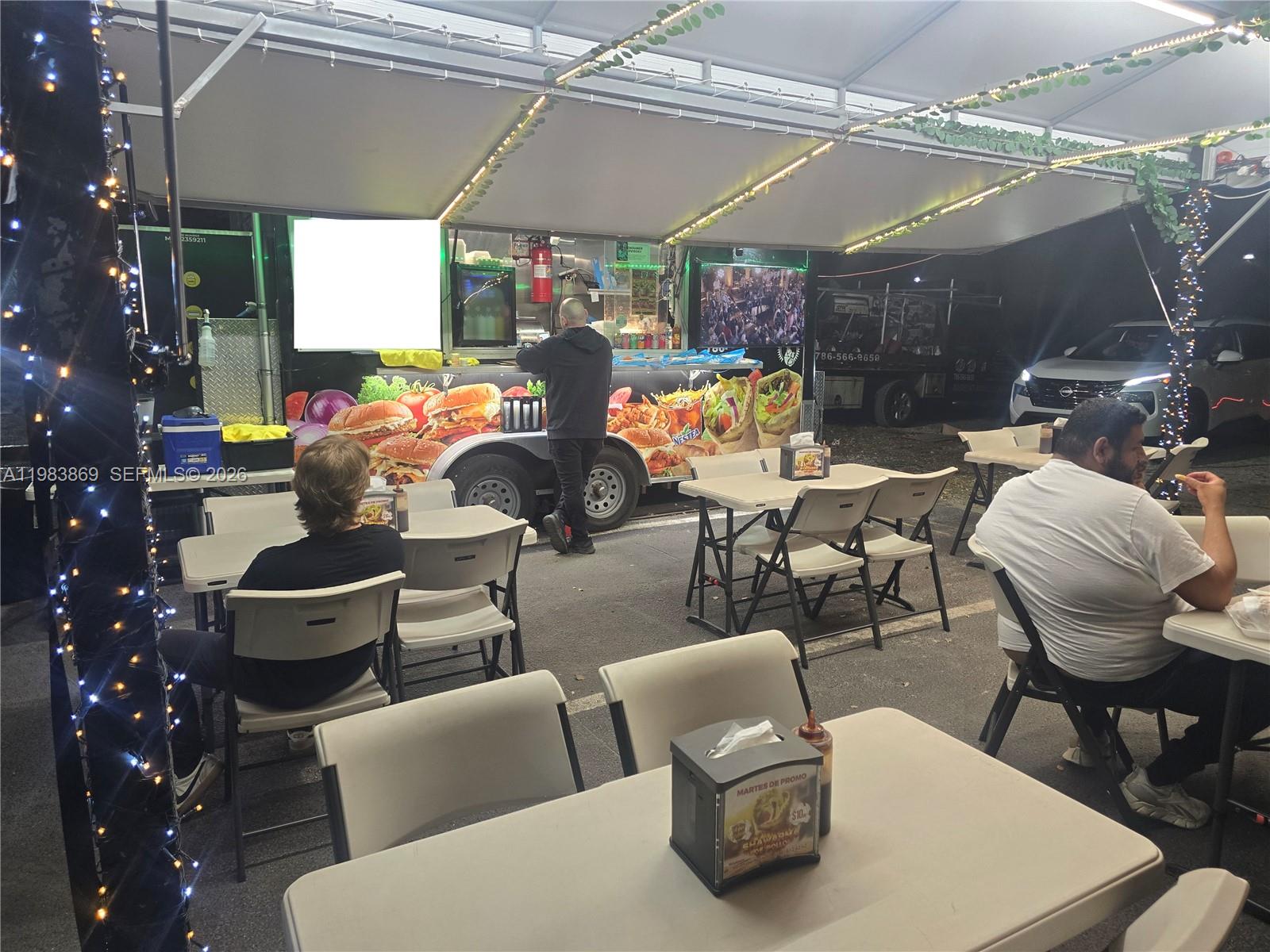An outdoor food truck setup features tables, chairs, and string lights under a canopy — 6439, Doral FL 33166, DORAL, FL