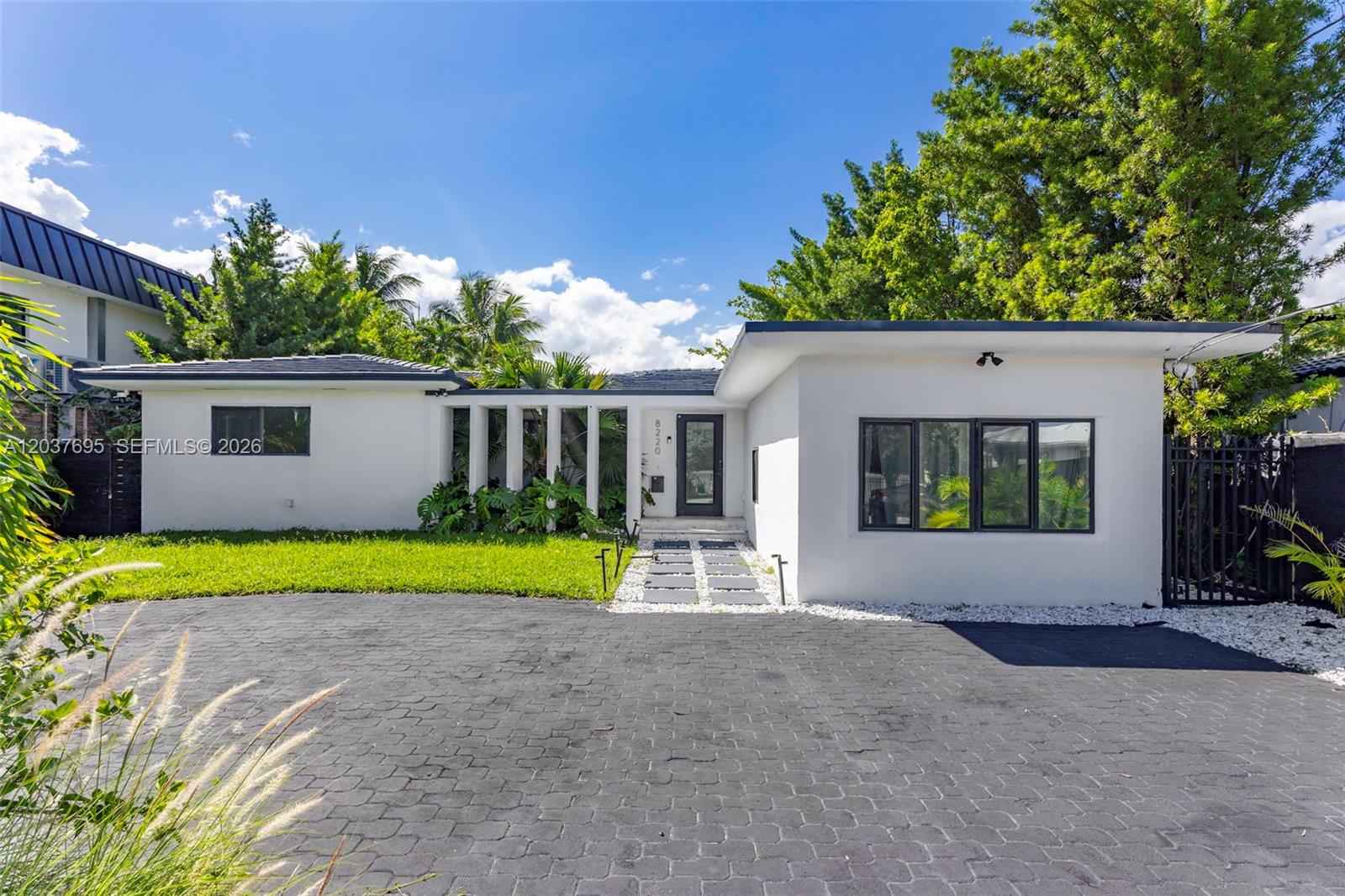A white single-story house features a dark paved driveway and a modern entryway — 8220 Hawthorne Ave, Miami Beach FL 33141, MIAMI BEACH, FL