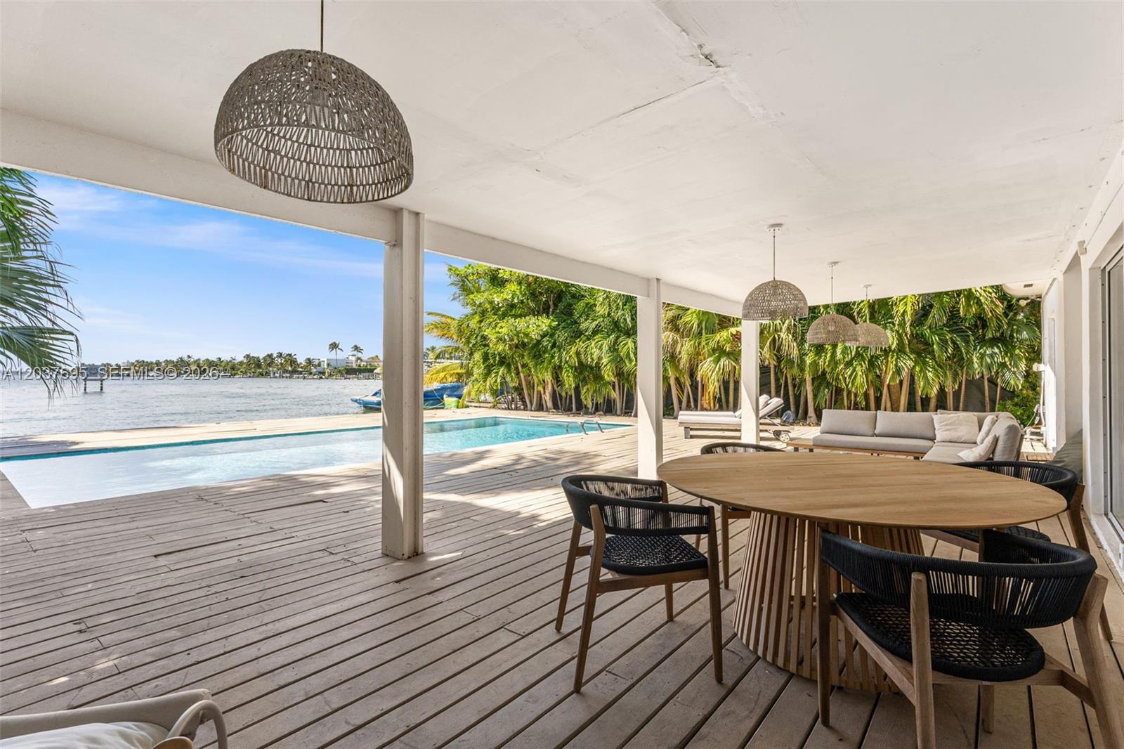 A covered wooden deck features a dining set, pool, and waterfront view — 8220 Hawthorne Ave, Miami Beach FL 33141, MIAMI BEACH, FL