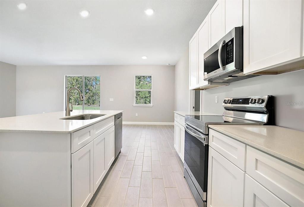 A modern kitchen features white cabinets, stainless steel appliances, and a central island with quartz countertops — 1814 DIPLOMAT PARKWAY W, CAPE CORAL, FL
