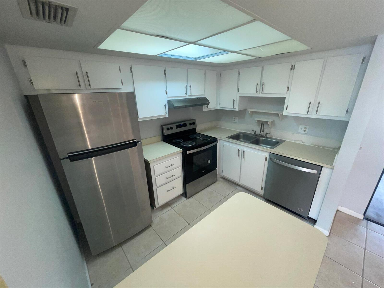 A kitchen features white cabinets, stainless steel appliances, tile flooring, and a drop ceiling light — 4185 Oak Terrace Drive, FL 33463, FL