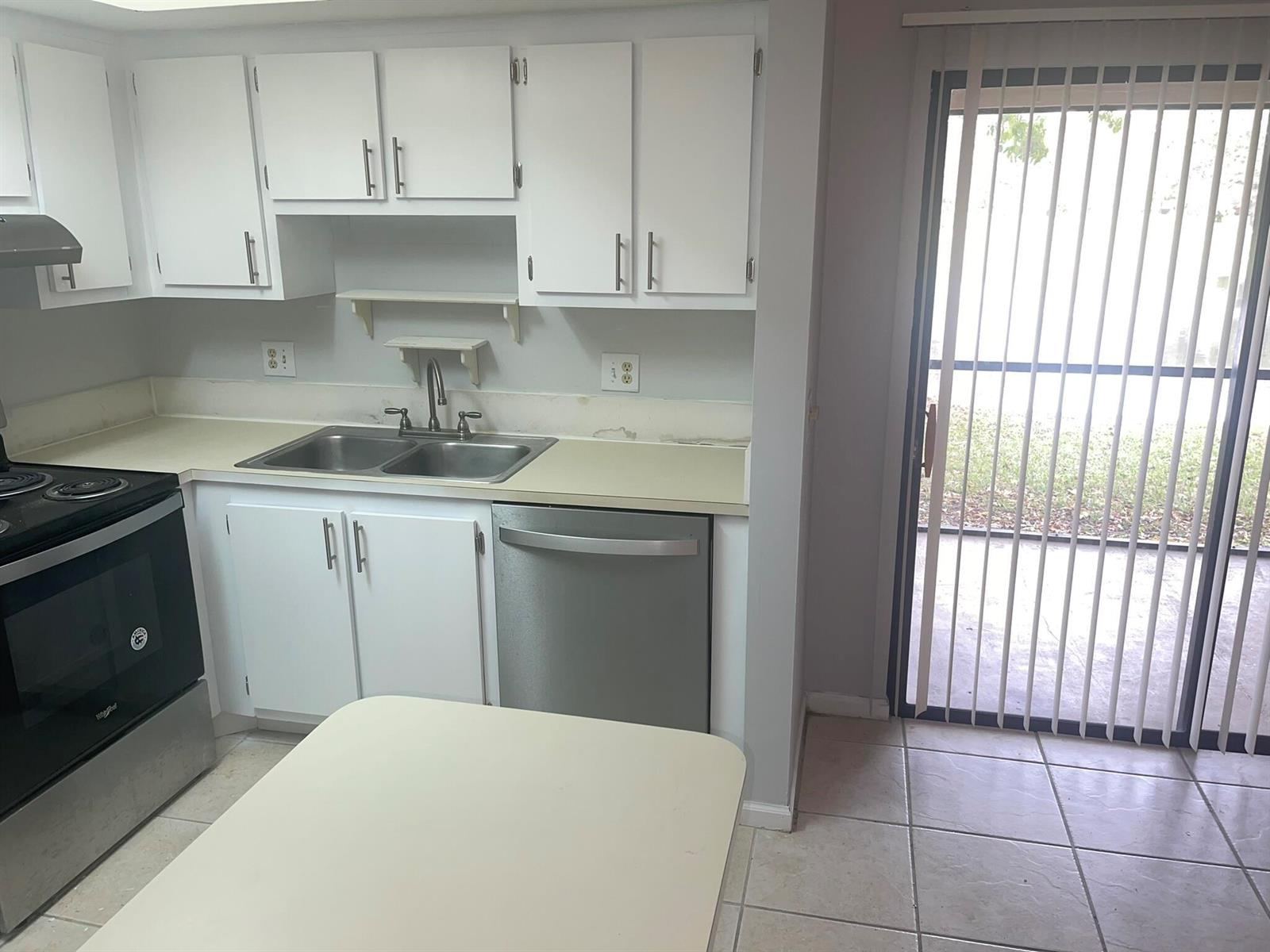 A kitchen features white cabinets, stainless steel appliances, a double sink, and a sliding glass door — 4185 Oak Terrace Drive, FL 33463, FL