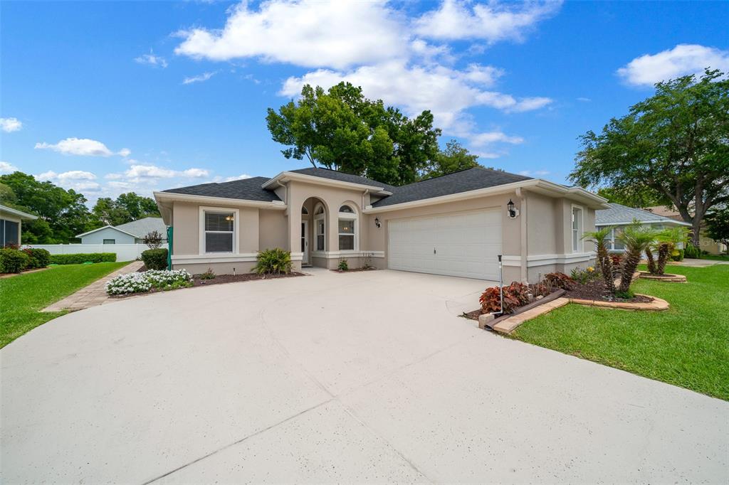 A single-story house with a beige stucco exterior, a two-car garage, and a concrete driveway — 10972 SW 69TH CIRCLE, OCALA, FL