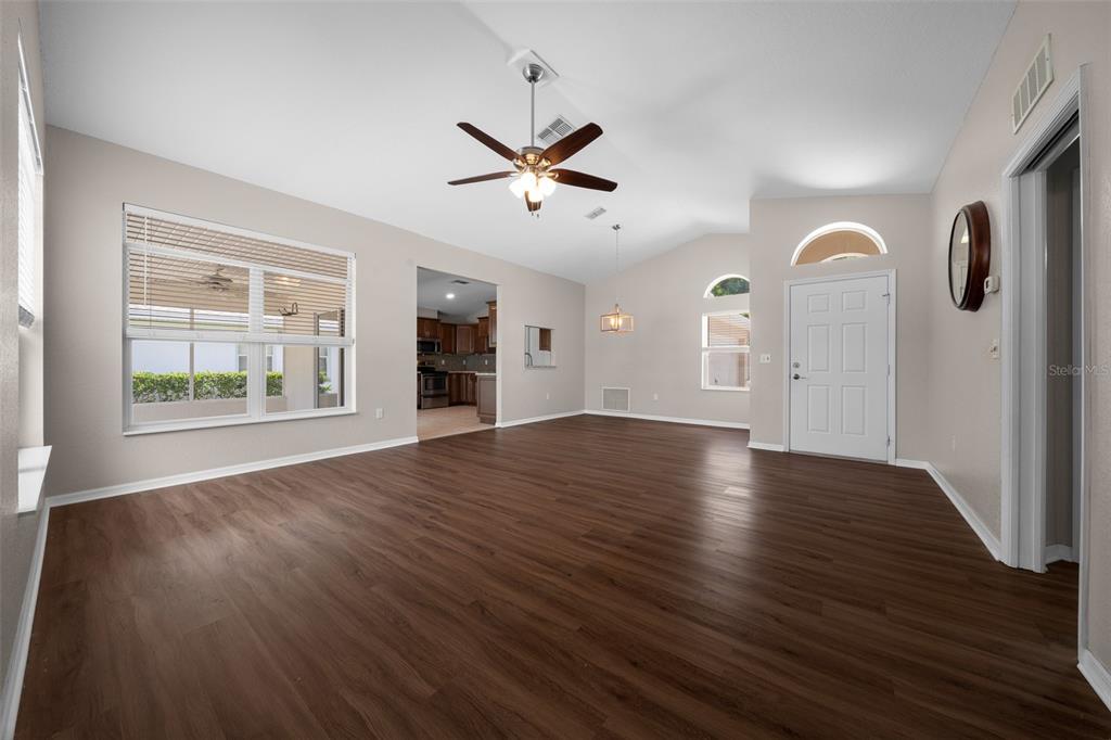 An empty living room features dark wood-look flooring, a ceiling fan, and a front door — 10972 SW 69TH CIRCLE, OCALA, FL