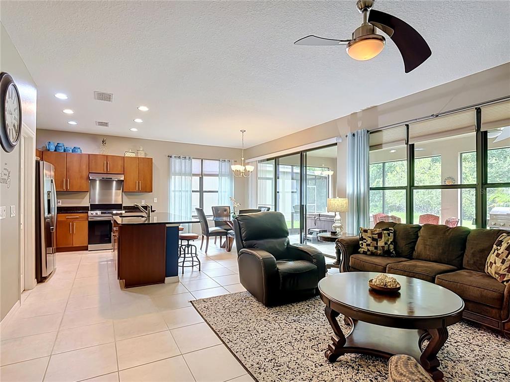 An open-concept living room and kitchen with tile floors, brown furniture, and sliding glass doors — 451 SCRIPPS RANCH RD, POINCIANA, FL