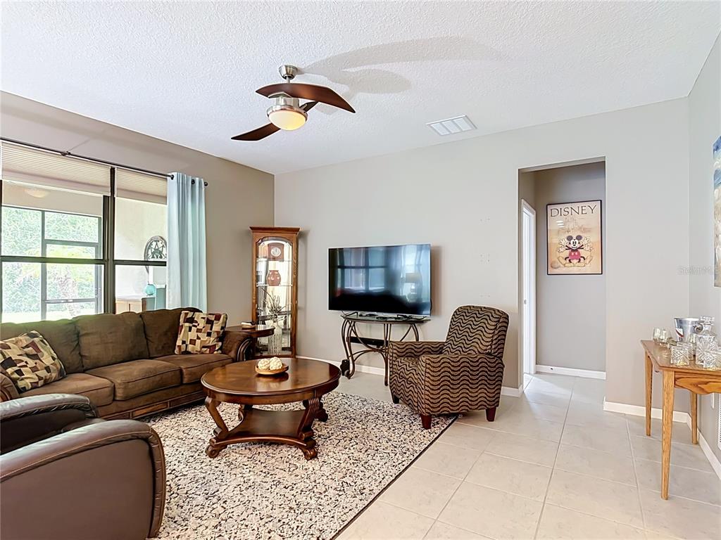 A living room features a brown sofa, patterned armchair, television, and a ceiling fan — 451 SCRIPPS RANCH RD, POINCIANA, FL