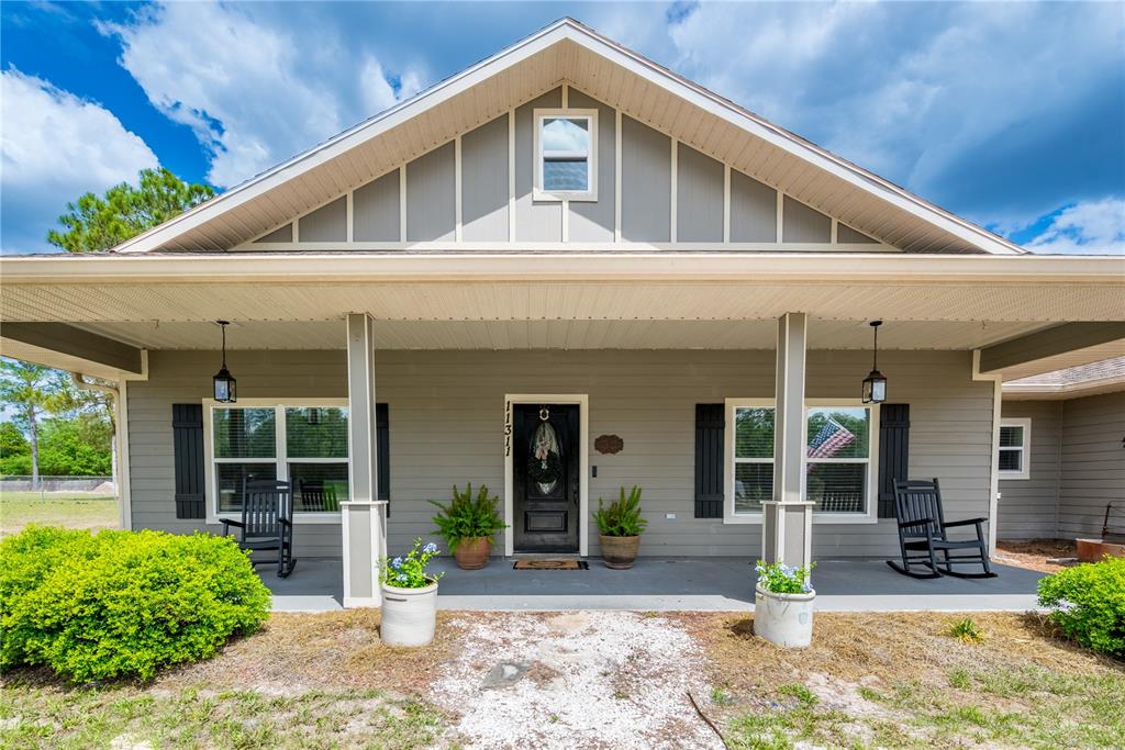 A gray house with a covered front porch, two rocking chairs, and a central entrance — 11311 NW 74TH COURT, CHIEFLAND, FL