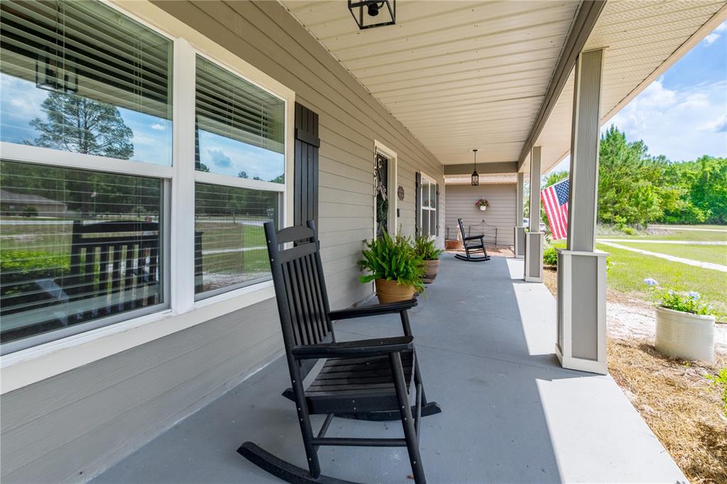 A covered front porch features gray siding, a concrete floor, and black rocking chairs — 11311 NW 74TH COURT, CHIEFLAND, FL