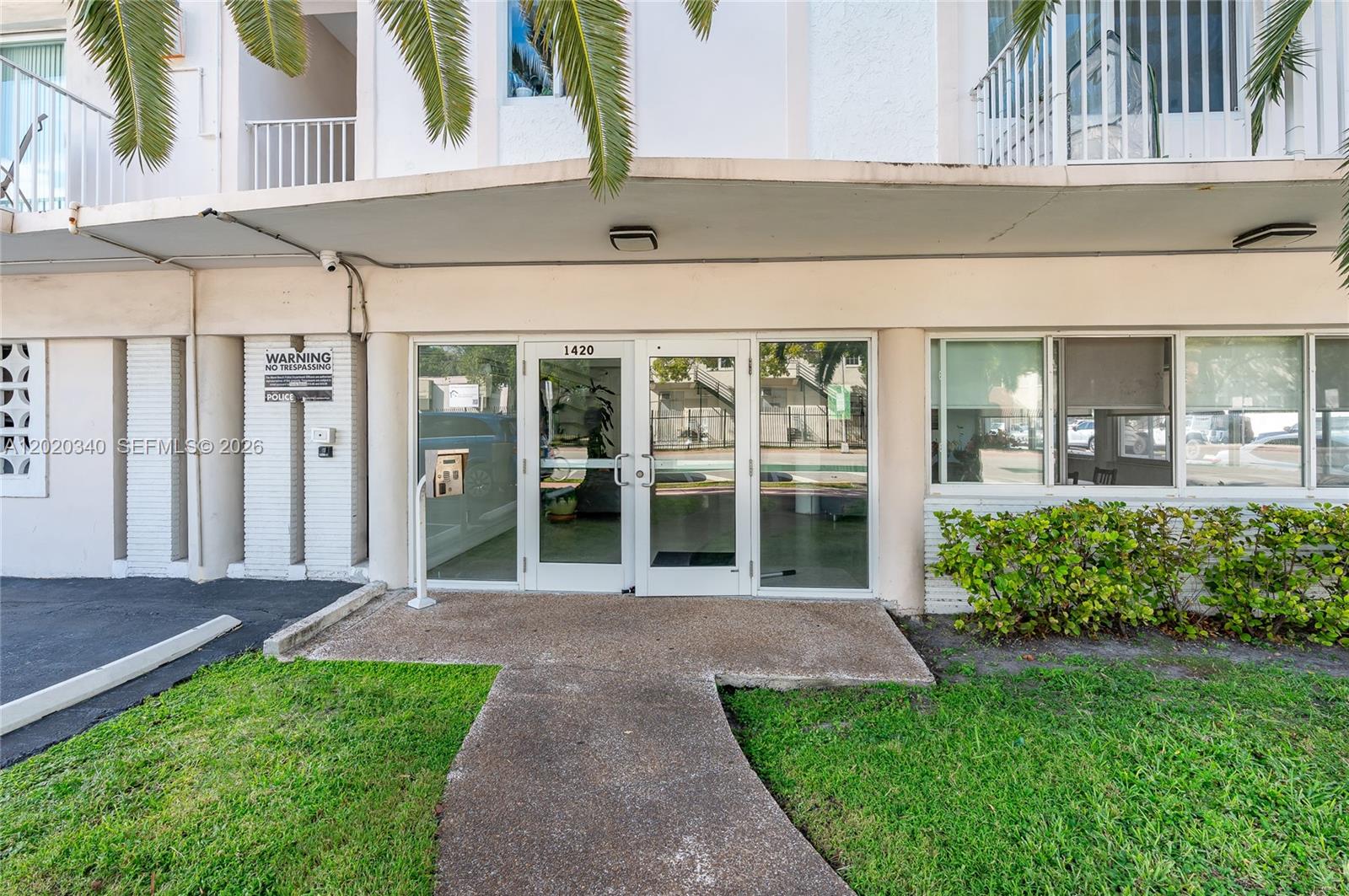 The exterior entrance of a multi-story building features glass double doors and a concrete walkway — 1420 Pennsylvania Ave # 201, Miami Beach FL 33139, MIAMI BEACH, FL