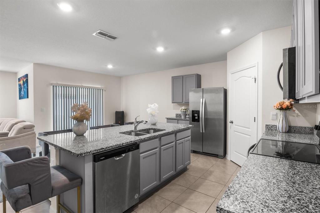 A kitchen features gray cabinetry, granite countertops, stainless steel appliances, and a central island — 1534 WAX MYRTLE WAY, HAINES CITY, FL