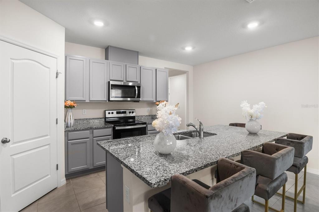 A kitchen features gray cabinets, granite countertops, a central island with seating, and stainless appliances — 1534 WAX MYRTLE WAY, HAINES CITY, FL