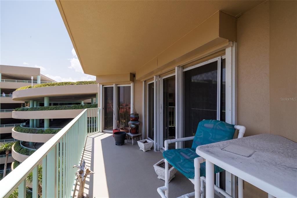 A balcony with a patio chair, table, and potted plants overlooks a multi-level parking garage — 4 OCEANS WEST BOULEVARD UNIT 601A, DAYTONA BEACH SHORES, FL