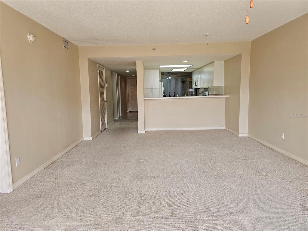 A carpeted living room opens to a kitchen with a breakfast bar and white cabinetry — 4 OCEANS WEST BOULEVARD UNIT 601A, DAYTONA BEACH SHORES, FL