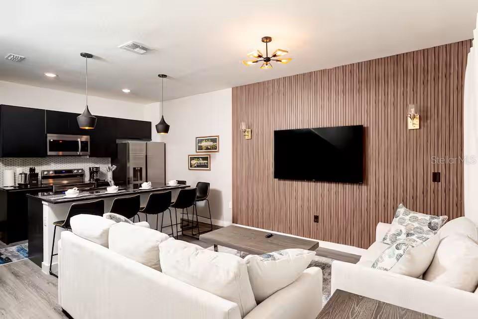 A modern open-concept living room features a wood-slatted accent wall and a kitchen island — 3261 ENERGY DRIVE, KISSIMMEE, FL