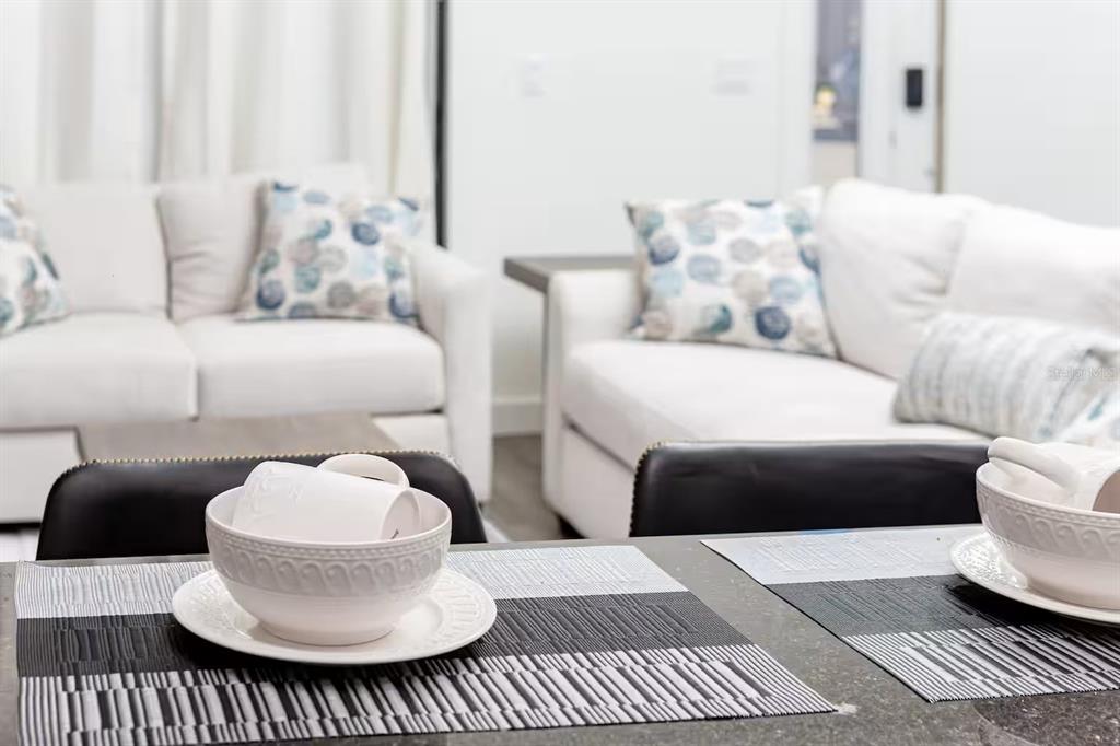 A dining table with place settings sits in the foreground before a bright living room — 3261 ENERGY DRIVE, KISSIMMEE, FL